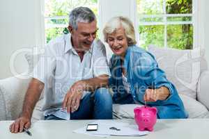 Senior woman putting coins in piggy bank while sitting with man