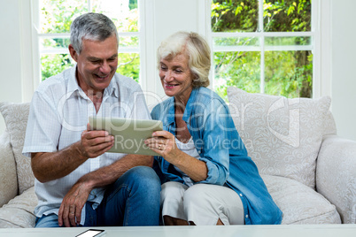 Happy senior couple holding digital tablet in sitting room
