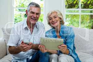 Portrait of senior couple with tablet and mobile phone in sittin