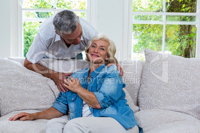 Senior woman touching husband hand while sitting on sofa