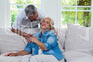 Senior woman touching husband hand while sitting on sofa