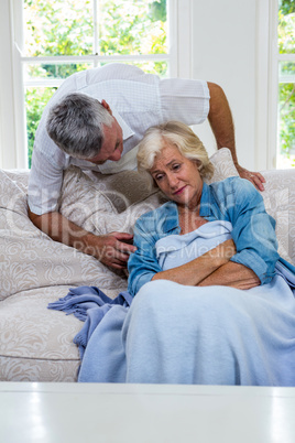 Husband talking to ill senior woman resting on sofa