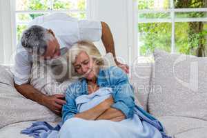 Senior man talking to ill wife resting on sofa