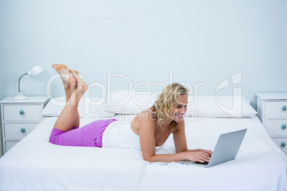 Side view of happy woman using laptop on bed
