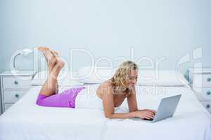 Side view of happy woman using laptop on bed