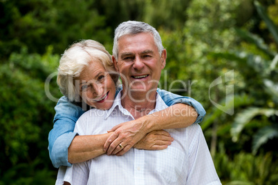 Senior woman embracing husband from behind against plants