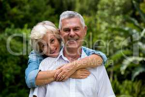 Senior woman embracing husband from behind against plants