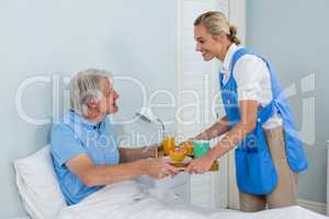 Nurse offering breakfast to senior man relaxing on bed