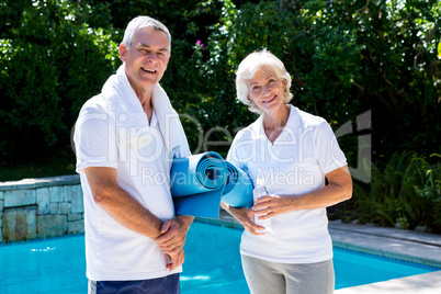Happy senior couple with exercise mats at poolside