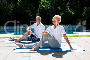 Senior couple exercising on mat at poolside