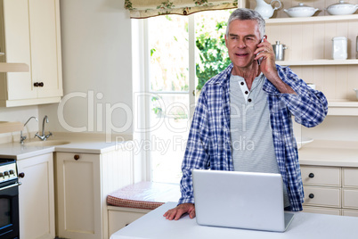 Senior man calling while standing in kitchen