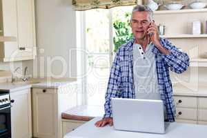 Senior man calling while standing in kitchen