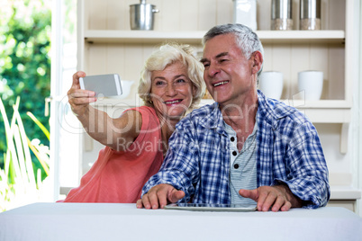 Senior couple taking selfie through mobile phone while sitting i