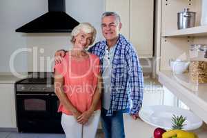 Smiling senior man with woman standing in kitchen at home