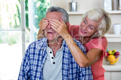 Senior woman hiding eyes of man in kitchen