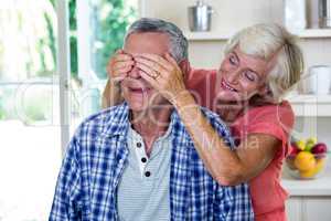 Senior woman hiding eyes of man in kitchen