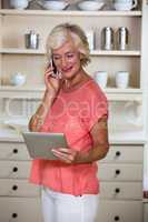 Senior woman using digital tablet and mobile phone in kitchen