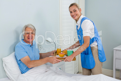 Nurse giving breakfast  to smiling senior man