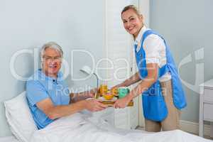 Nurse giving breakfast  to smiling senior man