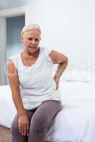 Senior woman suffering from back pain while sitting in bedroom