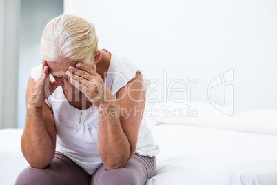 Senior woman with head in hand sitting at  bedroom