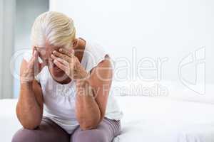 Senior woman with head in hand sitting at  bedroom