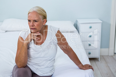 Upset senior woman sitting on bed in bedroom