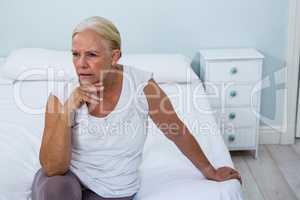 Upset senior woman sitting on bed in bedroom