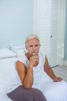 Upset senior woman with hand on chin sitting on bed