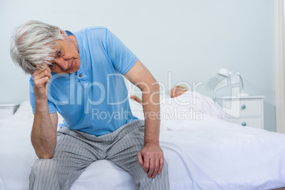 Upset senior man touching head while woman sleeping on bed