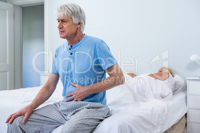 Senior man having stomach pain while sitting on bed