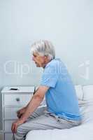 Side view of thoughtful senior man sitting on bed
