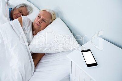 Senior couple sleeping on bed with phone on table