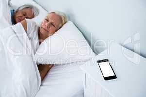 Senior couple sleeping on bed with phone on table