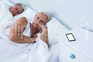 Thoughtful senior woman relaxing on bed with phone on table