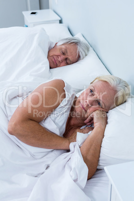 Thoughtful senior woman lying on bed