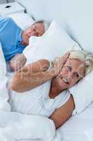 Senior woman covering ears while man snoring