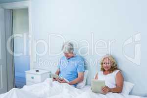 Retired couple using digital tablets while sitting on bed