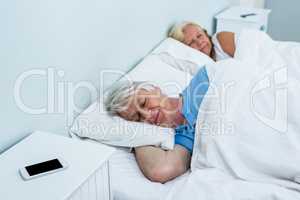 Senior couple resting on bed with phone on table
