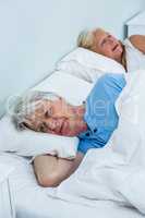 Thoughtful senior man relaxing on bed while woman snoring
