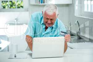 Senior man using laptop on kitchen counter