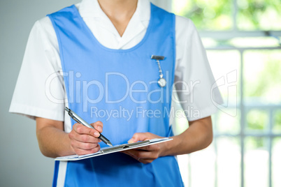 Midsection of nurse writing on clipboard