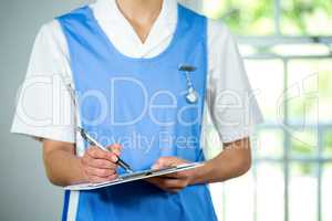 Midsection of nurse writing on clipboard