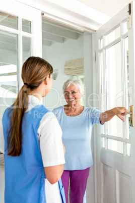 Smiling senior woman standing with nurse by door