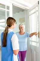 Smiling senior woman standing with nurse by door