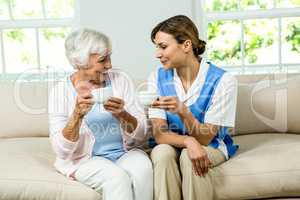 Smiling nurse and senior woman holding coffee cups