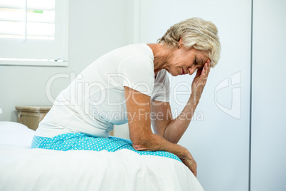 Tensed aged woman sitting on bed