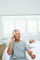 Old man talking on phone with woman sleeping