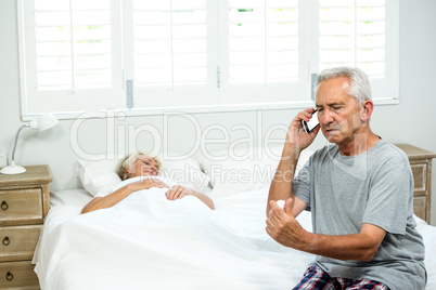 Aged man talking on mobile phone with senior woman relaxing