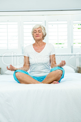 Aged woman doing yoga on bed